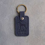 Blueberry navy leather keychain debossed with a Doberman silhouette and the words Dobie DAD, on gray concrete