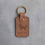 Caramel leather keychain debossed with a dog shaking off water drops above DOCK DOG, on gray concrete