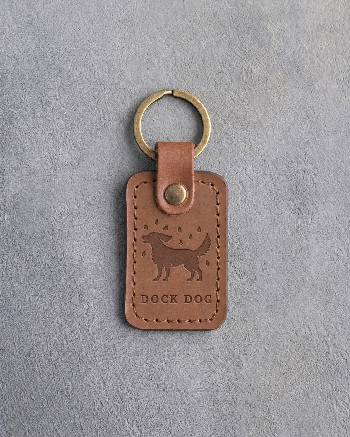 Caramel leather keychain debossed with a dog shaking off water drops above DOCK DOG, on gray concrete