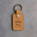 Indian Summer tan leather keychain debossed with a bone-shaped cake and candle above Milo and TURNS THREE, on gray concrete
