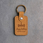 Indian Summer tan leather keychain debossed with a bone-shaped cake and candle above Happy birthday and GOOD DOG, on gray concrete