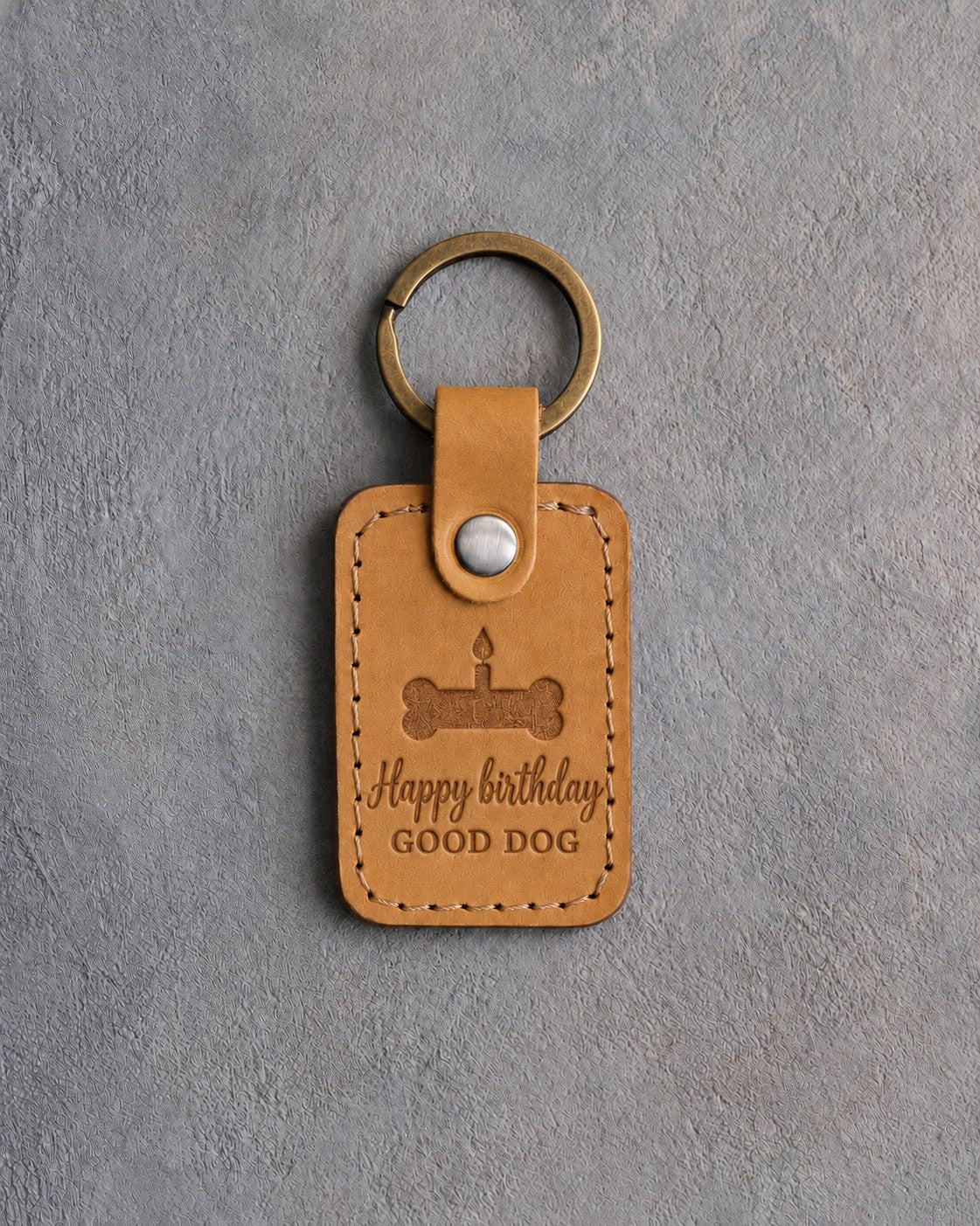 Indian Summer tan leather keychain debossed with a bone-shaped cake and candle above Happy birthday and GOOD DOG, on gray concrete