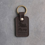 Dark espresso leather keychain debossed with a pug lying head up above My pug and EVER FAITHFUL, on gray concrete
