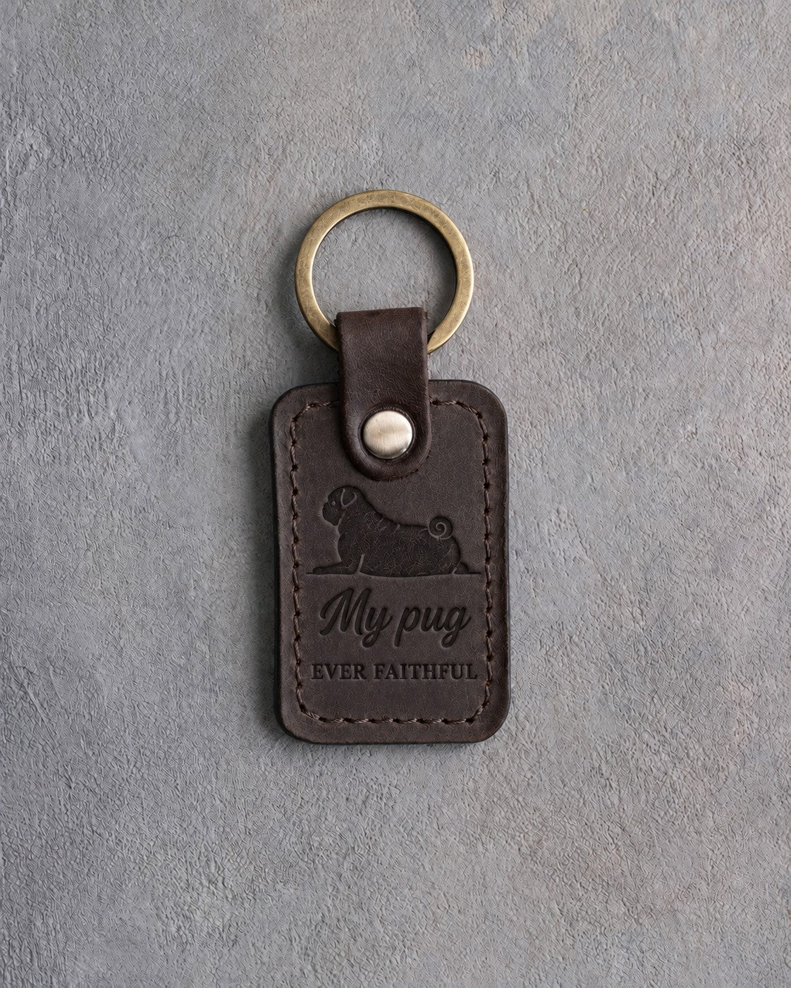 Dark espresso leather keychain debossed with a pug lying head up above My pug and EVER FAITHFUL, on gray concrete