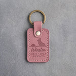 Parisian Blossom pink leather keychain debossed with a corgi seated on a horizon facing a low sun above Winston, 2013 · 2025 and ALWAYS, on gray concrete