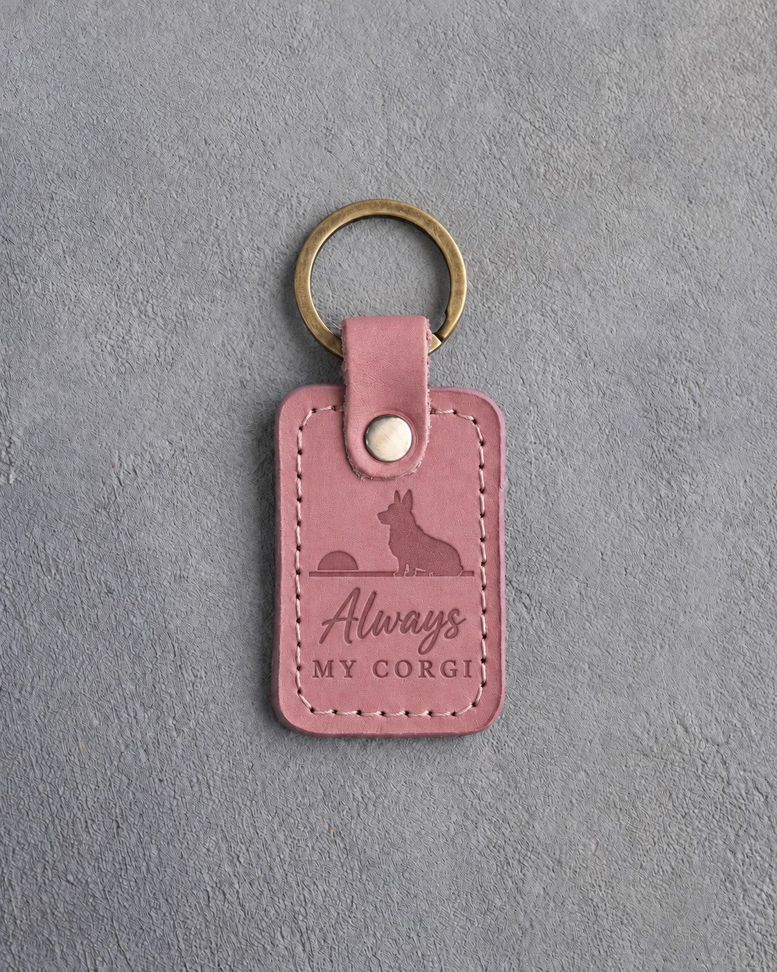 Parisian Blossom pink leather keychain debossed with a corgi seated on a horizon facing a low sun above Always and MY CORGI, on gray concrete