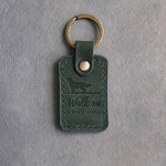 Forest green leather keychain debossed with a golden retriever walking off a long ground line above Walk on and GOOD DOG, on gray concrete