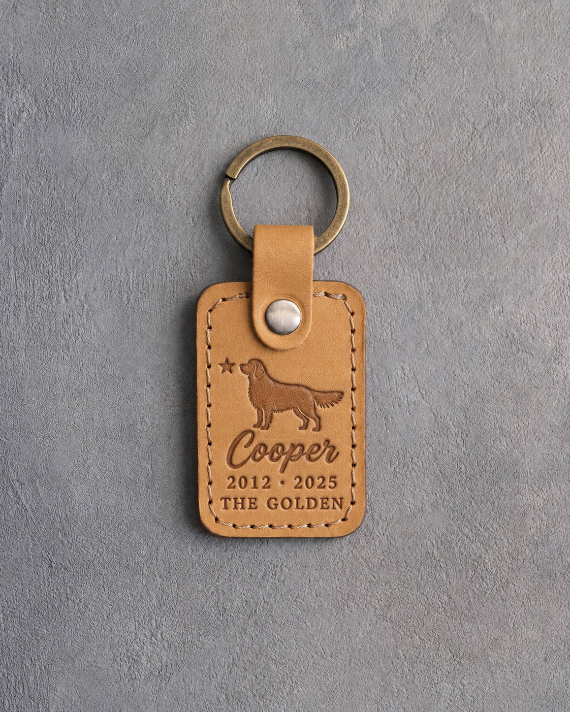 Indian Summer tan leather keychain debossed with a golden retriever and a small star above Cooper, 2012 · 2025 and THE GOLDEN, on gray concrete