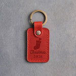Poppy red leather keychain debossed with a Christmas stocking holding a dog bone above Christmas and 2026, on gray concrete
