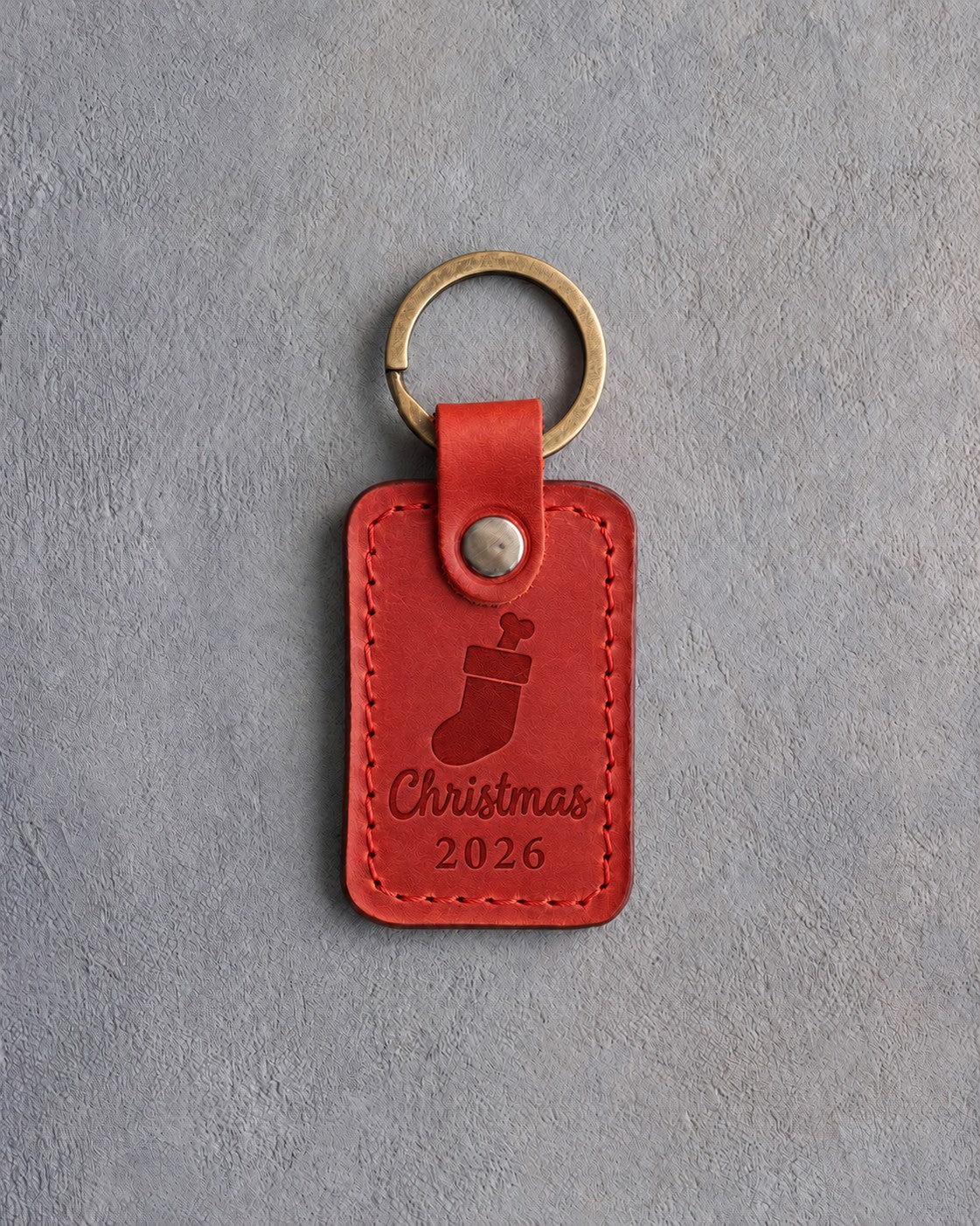 Poppy red leather keychain debossed with a Christmas stocking holding a dog bone above Christmas and 2026, on gray concrete