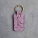 Lilac leather keychain debossed with a sitting mixed-breed dog and the words Dog GRANDMA, on gray concrete