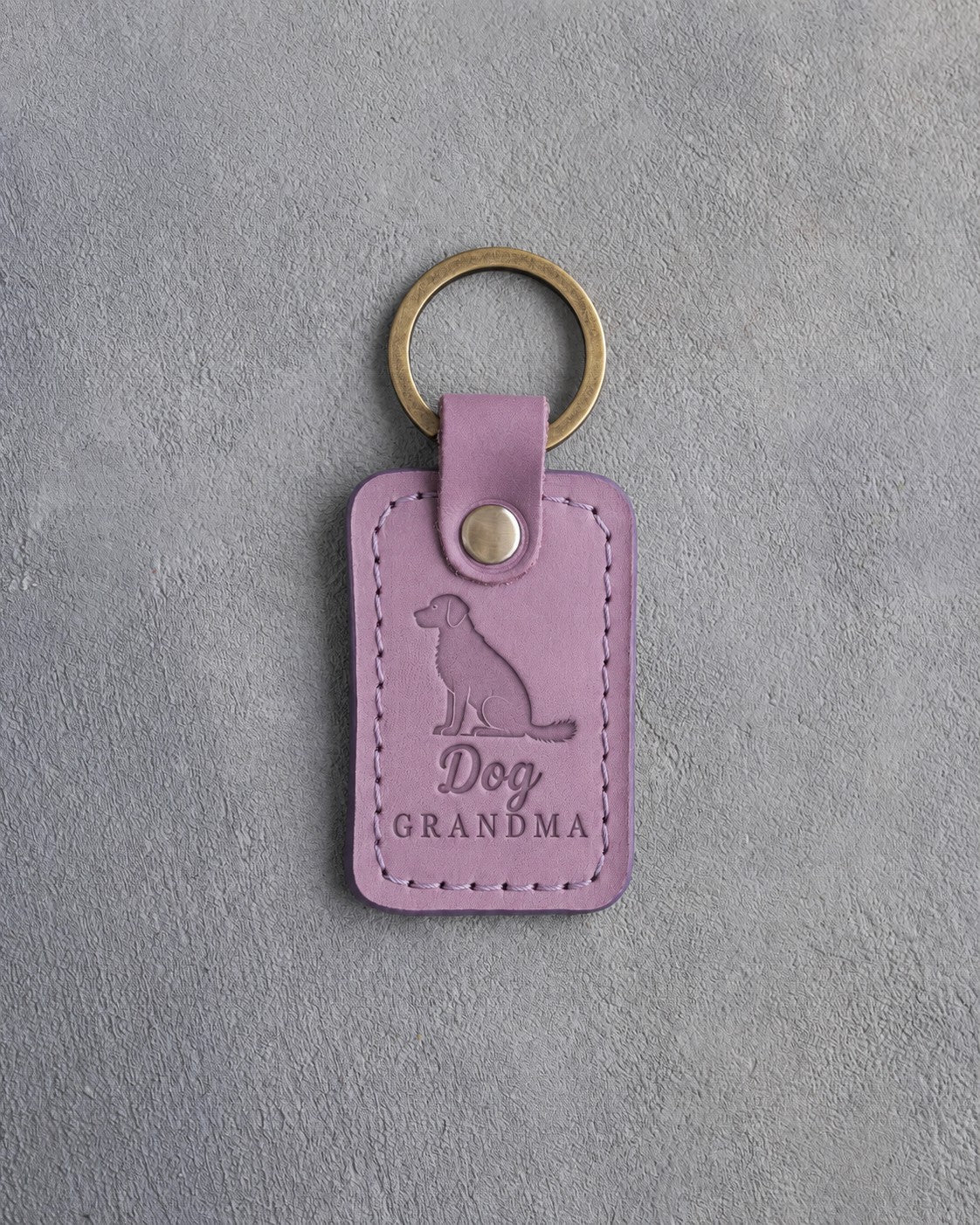 Lilac leather keychain debossed with a sitting mixed-breed dog and the words Dog GRANDMA, on gray concrete
