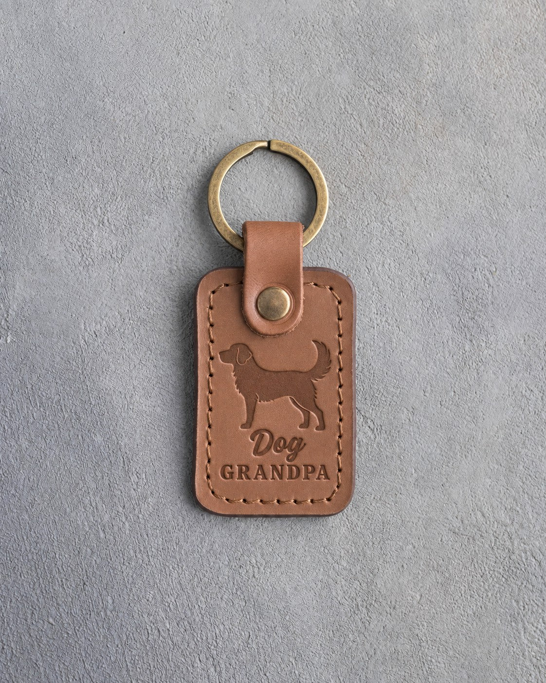 Caramel leather keychain debossed with a standing mixed-breed dog and the words Dog GRANDPA, on gray concrete