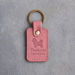 Parisian Blossom pink leather keychain debossed with a maltipoo above Thank you and GROOMER, on gray concrete