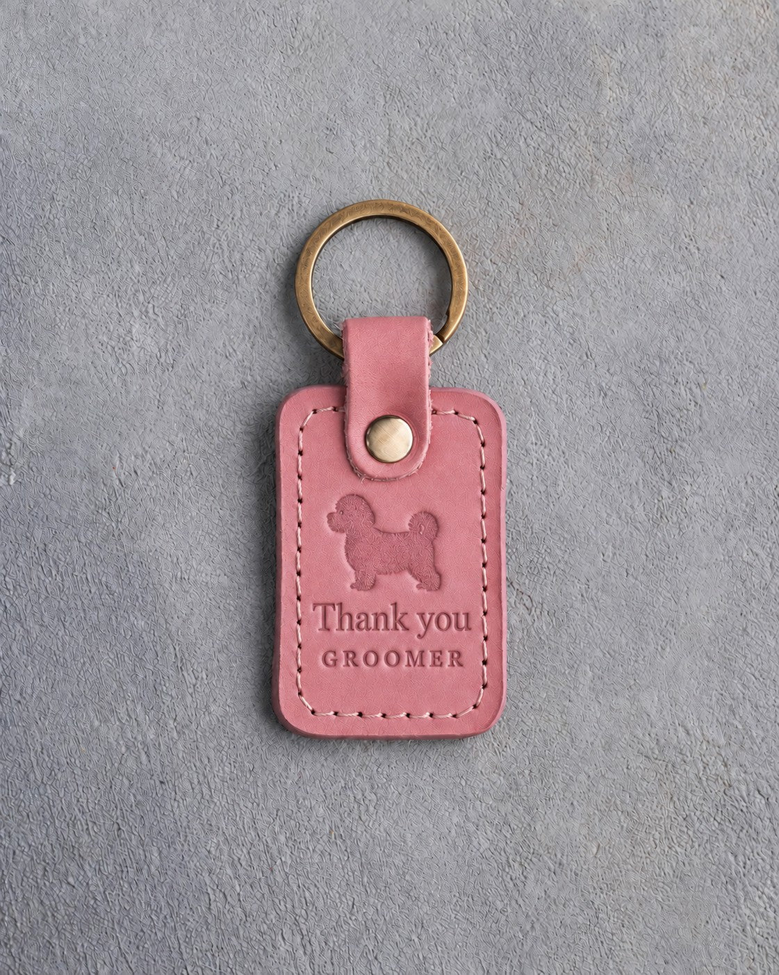 Parisian Blossom pink leather keychain debossed with a maltipoo above Thank you and GROOMER, on gray concrete