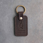 Dark espresso leather keychain debossed with an empty dog collar on a hook above Forever and GOOD DOG, on gray concrete
