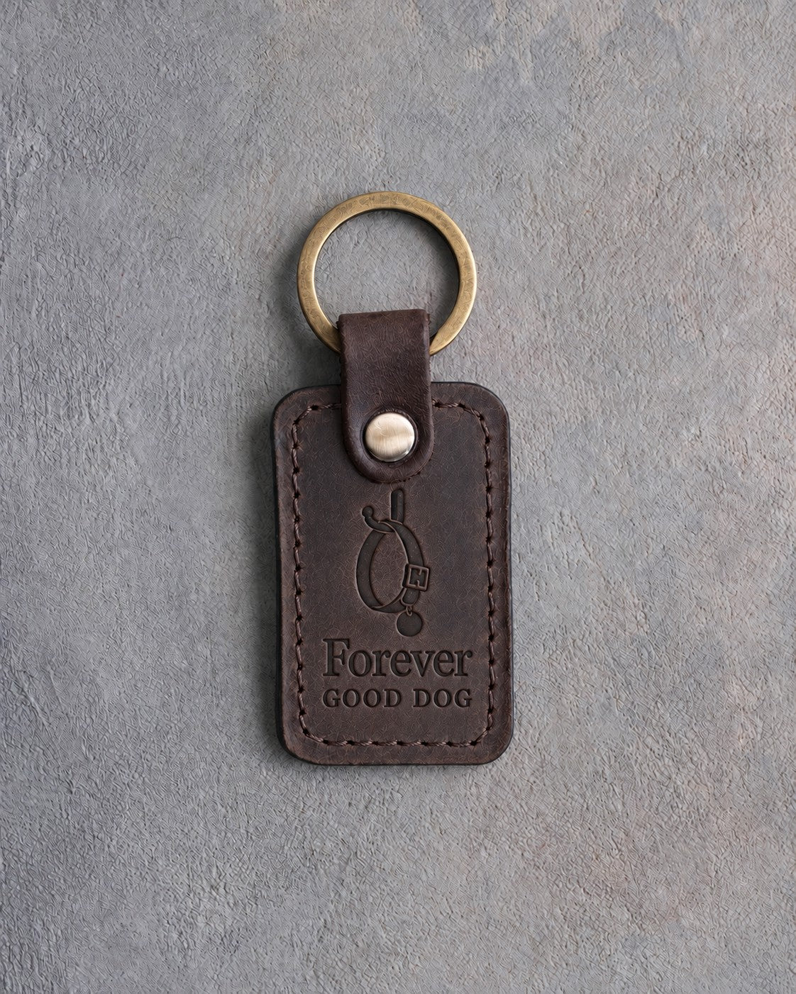 Dark espresso leather keychain debossed with an empty dog collar on a hook above Forever and GOOD DOG, on gray concrete