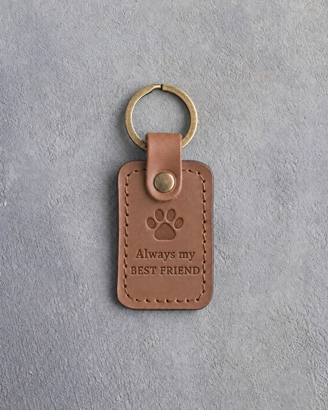 Caramel leather keychain debossed with a single paw print above Always my and BEST FRIEND, on gray concrete