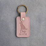Blush pink leather keychain debossed with a sitting mixed-breed dog above the words Dog MOM, on gray concrete