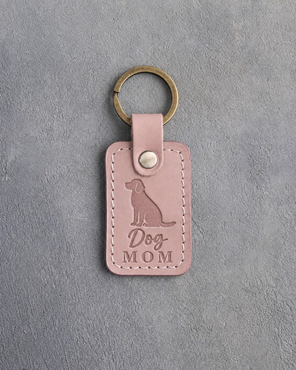 Blush pink leather keychain debossed with a sitting mixed-breed dog above the words Dog MOM, on gray concrete
