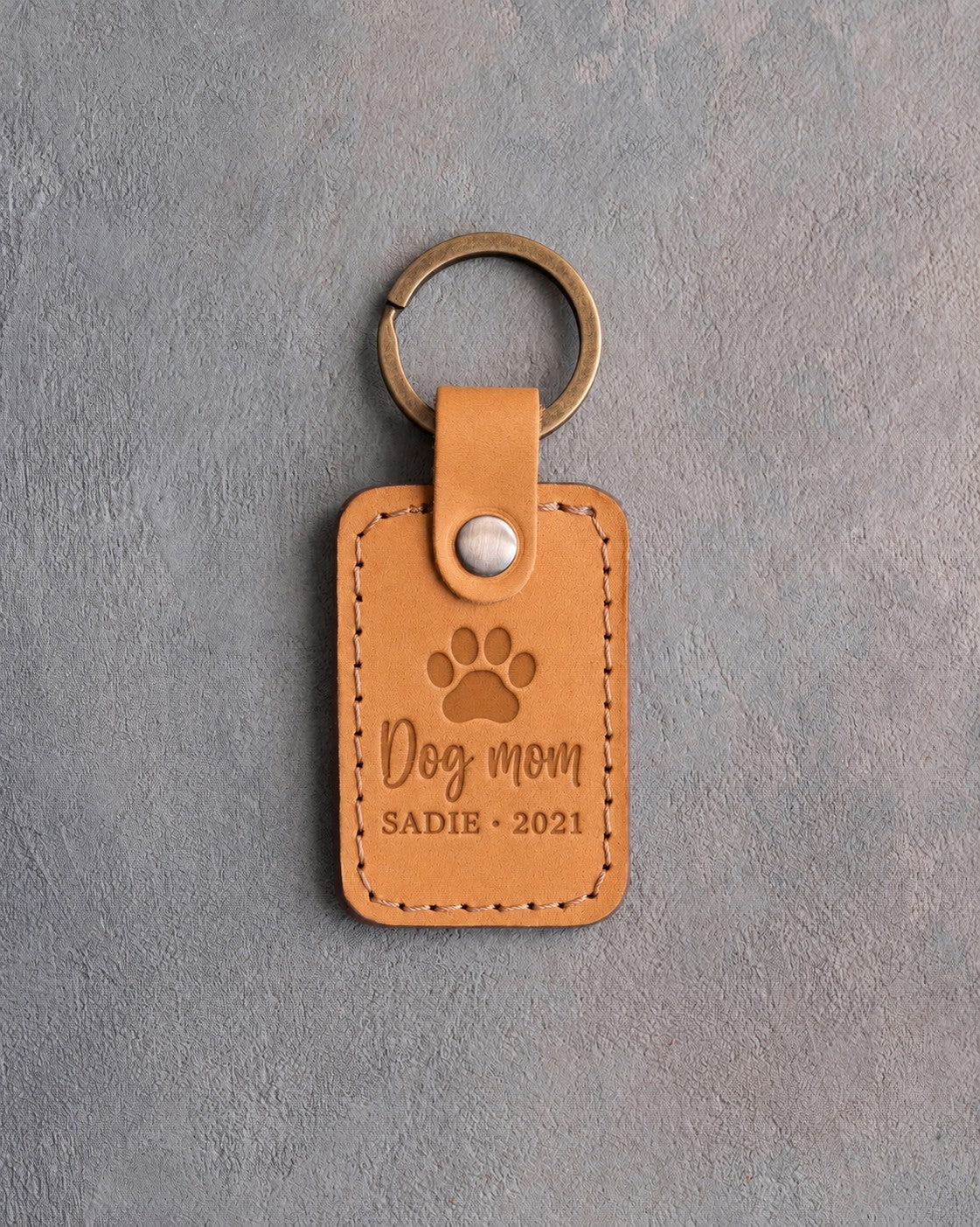 Indian Summer tan leather keychain debossed with a paw print above Dog mom and SADIE · 2021, on gray concrete