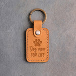 Indian Summer tan leather keychain debossed with a paw print above Dog mom and FOR LIFE, on gray concrete