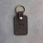 Dark espresso leather keychain debossed with a Labrador above Milo and HOME 3·14·24, on gray concrete