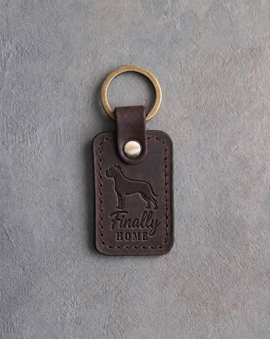 Dark espresso leather keychain debossed with a pit bull above Finally and HOME, on gray concrete