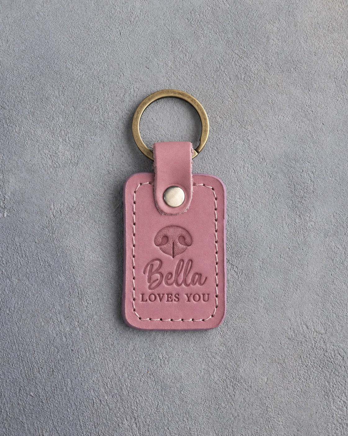 Parisian Blossom pink leather keychain debossed with a dog nose print above Bella and LOVES YOU, on gray concrete
