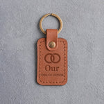 Caramel leather keychain debossed with two interlocked wedding rings above Our and DOG OF HONOR, on gray concrete