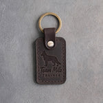 Dark espresso leather keychain debossed with a Labrador above Team Milo and TRAINER, on gray concrete