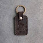 Dark espresso leather keychain debossed with a German shepherd above Thank you and TRAINER, on gray concrete