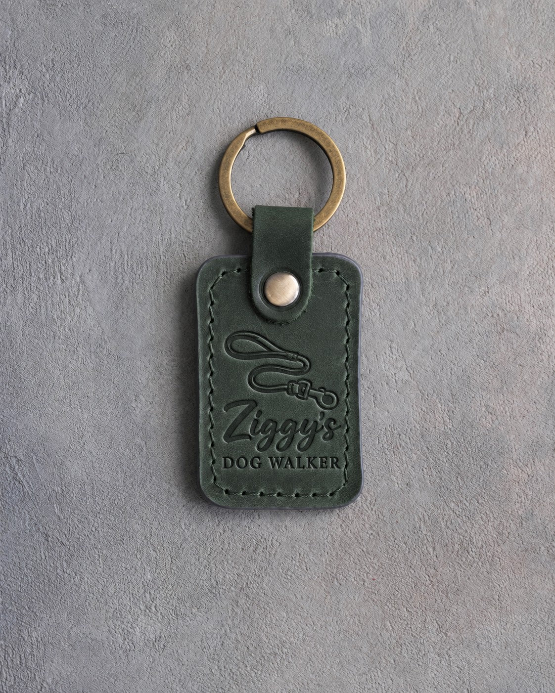 Forest green leather keychain debossed with a looping leash above Ziggy's and DOG WALKER, on gray concrete