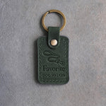 Forest green leather keychain debossed with a looping leash above Favorite and DOG WALKER, on gray concrete