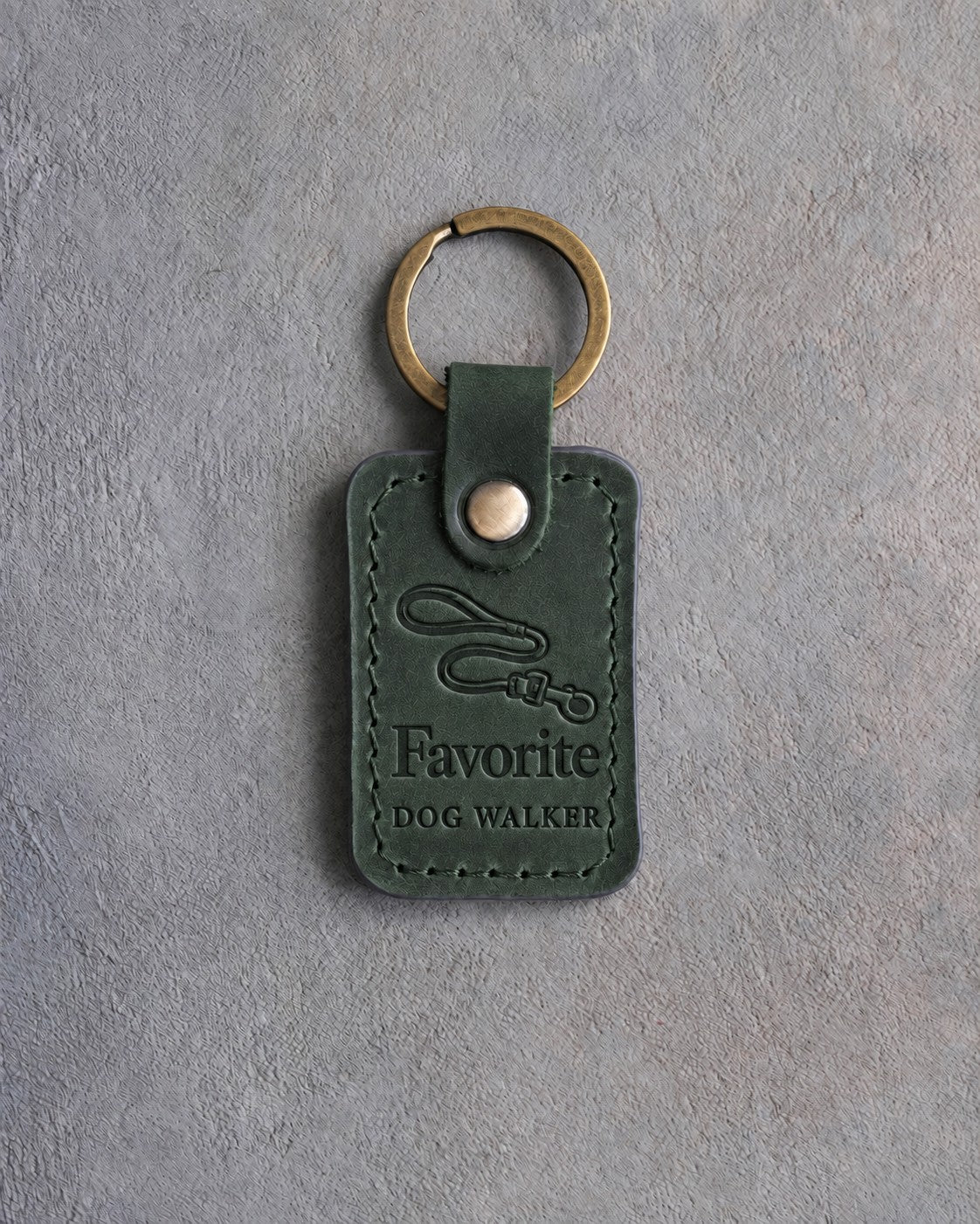 Forest green leather keychain debossed with a looping leash above Favorite and DOG WALKER, on gray concrete