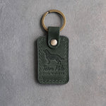 Forest green leather keychain debossed with a golden retriever above Team Milo and DOG WALKER, on gray concrete
