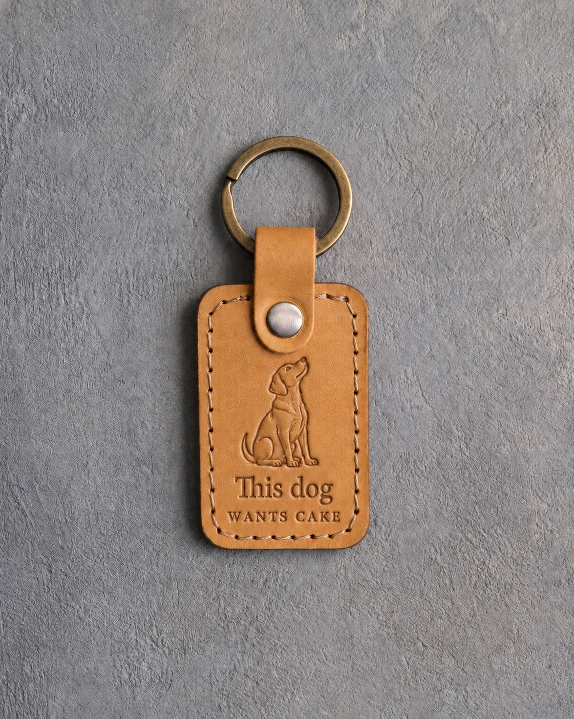 Indian Summer tan leather keychain debossed with a begging dog above This dog and WANTS CAKE, on gray concrete