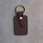 Dark espresso leather keychain debossed with a sitting dog looking up above The dog's and CHAUFFEUR, on gray concrete
