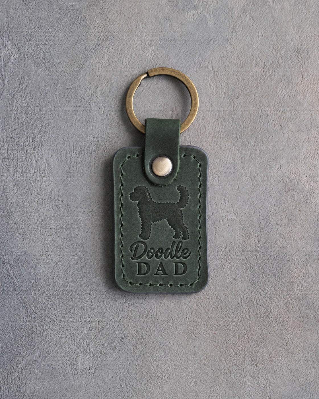 Forest green leather keychain debossed with a goldendoodle silhouette and Doodle DAD, on gray concrete