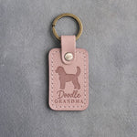 Blush pink leather keychain debossed with a goldendoodle silhouette and the words Doodle GRANDMA, on gray concrete