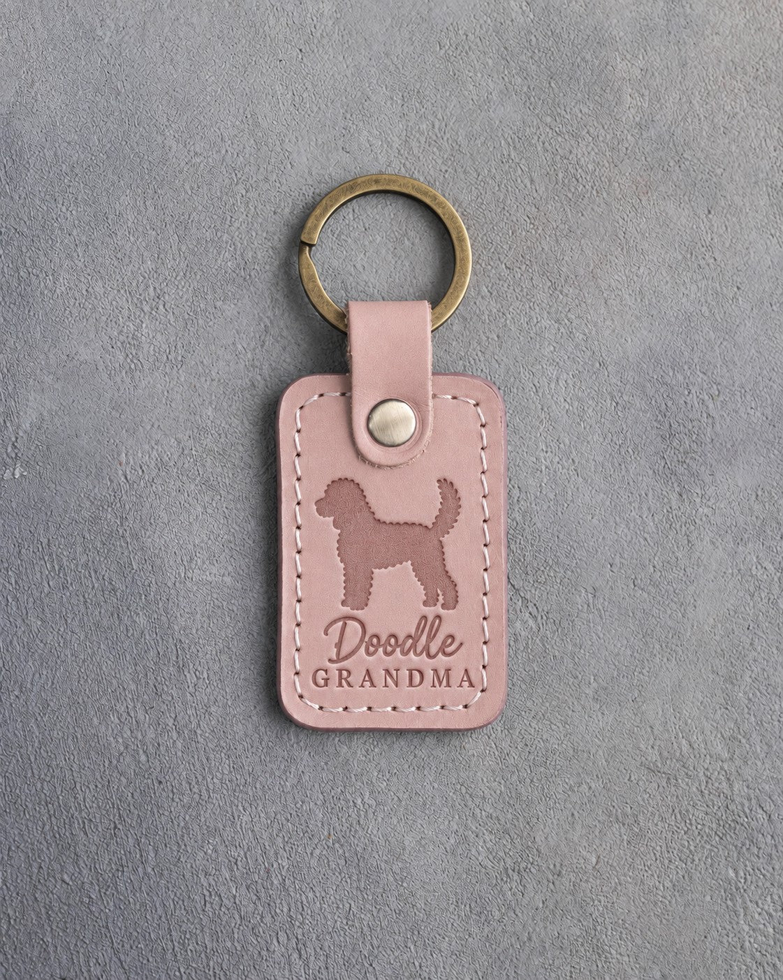 Blush pink leather keychain debossed with a goldendoodle silhouette and the words Doodle GRANDMA, on gray concrete