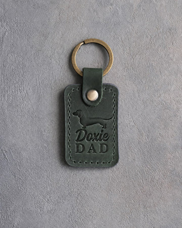 Forest green leather keychain with a debossed dachshund and Doxie DAD lettering on gray concrete