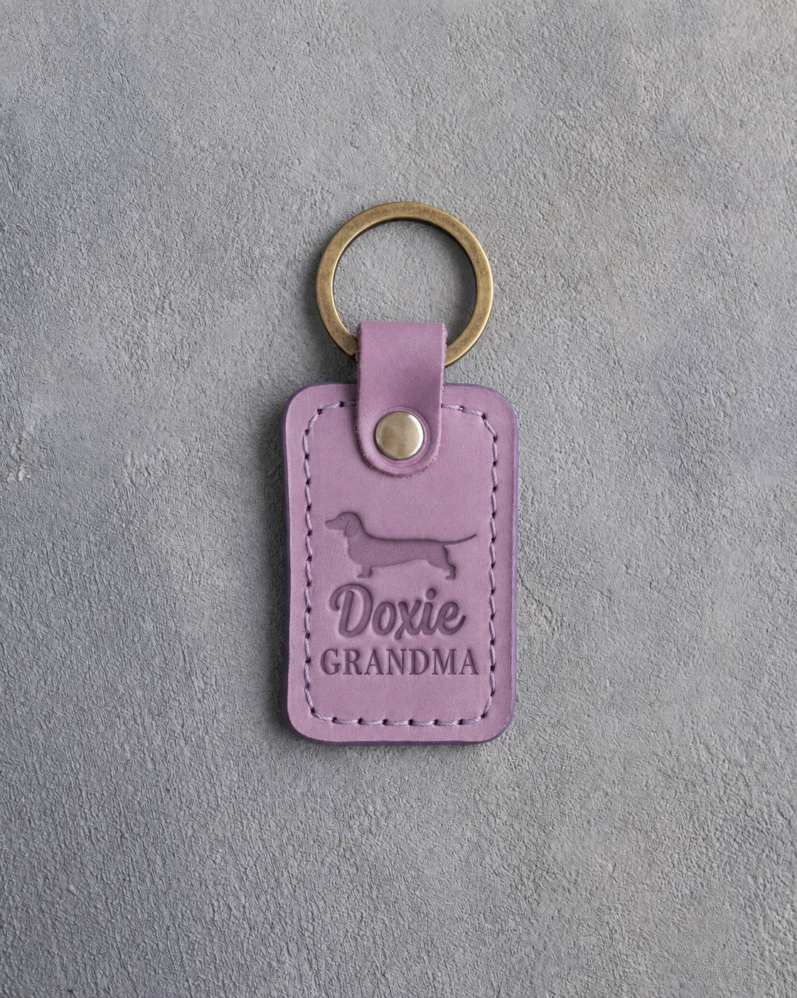 Lilac leather keychain debossed with a dachshund silhouette and the words Doxie GRANDMA, on gray concrete