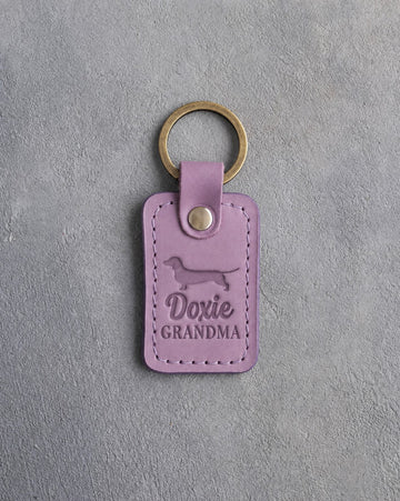 Lilac leather keychain debossed with a dachshund silhouette and the words Doxie GRANDMA, on gray concrete