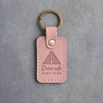 Blush pink leather keychain debossed with a road to the horizon above Drive safe and COME HOME