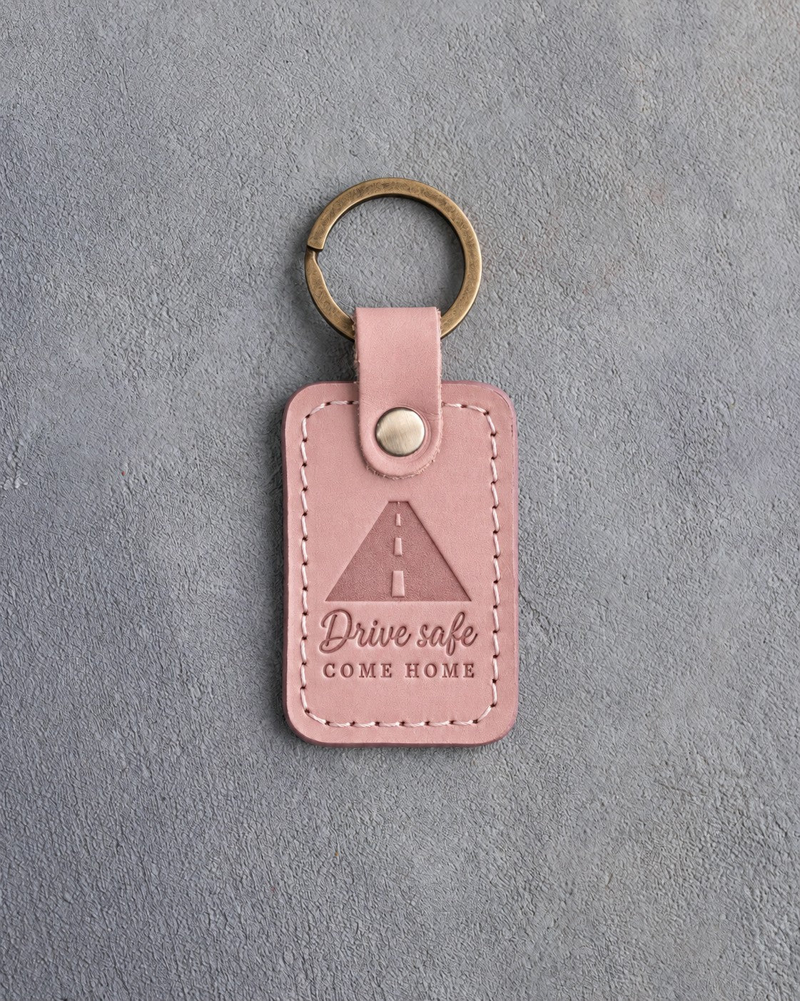 Blush pink leather keychain debossed with a road to the horizon above Drive safe and COME HOME
