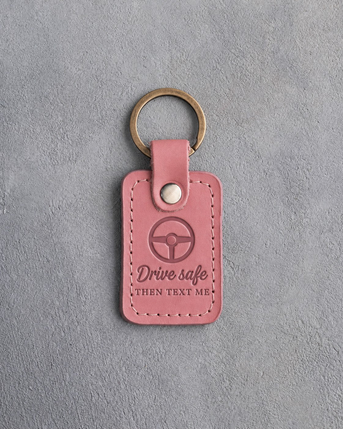 Rose pink leather keychain debossed with a steering wheel above Drive safe and THEN TEXT ME