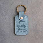 Turquoise leather keychain debossed with a golf cart above the words Drives THE CART, on gray plaster