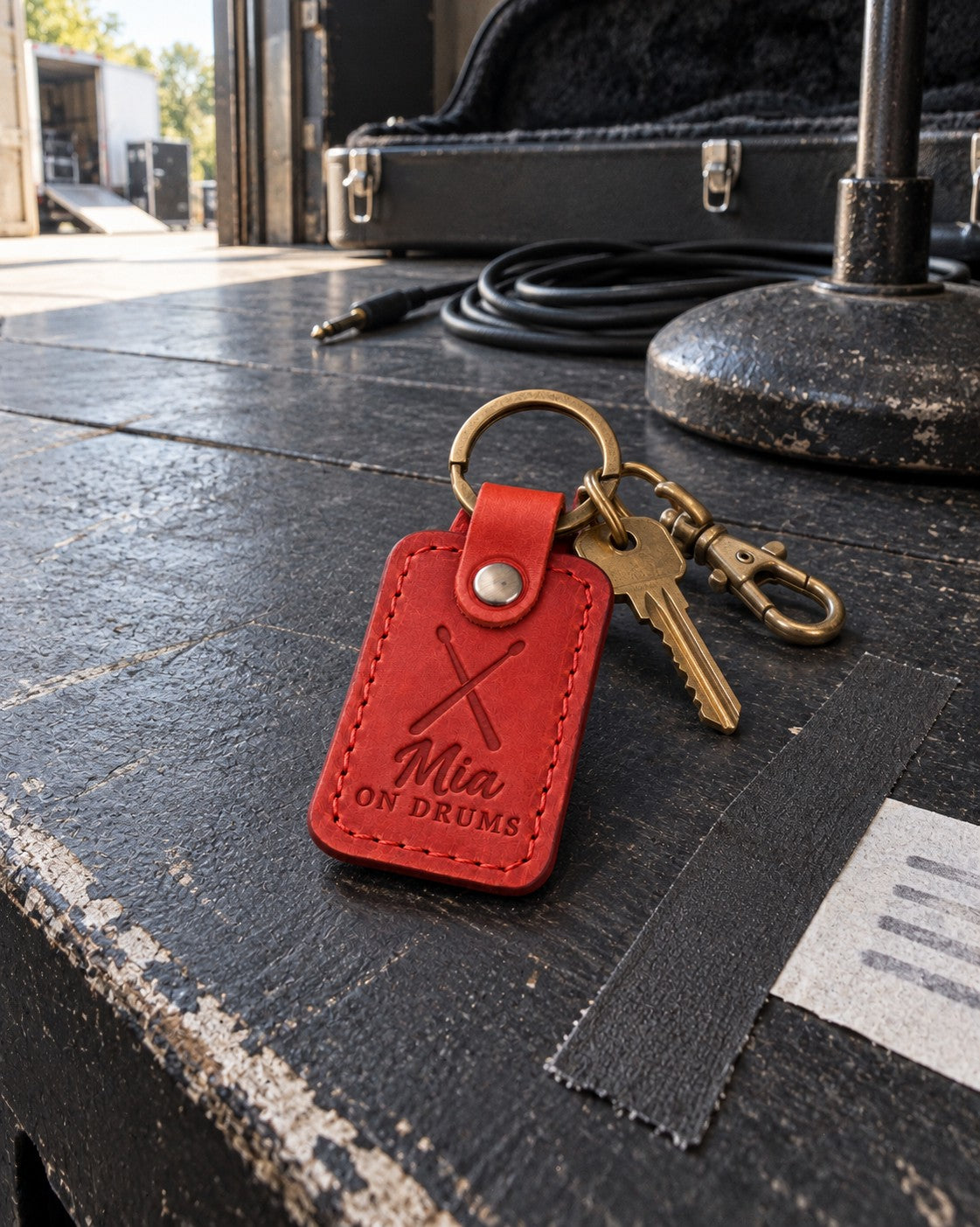 Mia ON DRUMS keychain in bright red leather hanging from a stick bag beside a snare drum