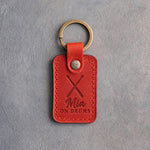 Poppy red leather keychain debossed with crossed drumsticks above the name Mia and ON DRUMS, on gray plaster